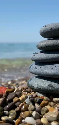 This phone live wallpaper depicts a stack of rocks on a serene beach, surrounded by the majestic ocean and a clear blue sky