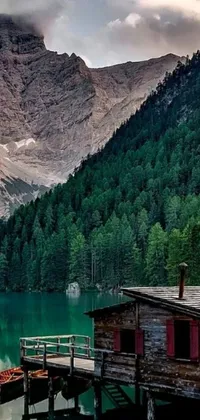 Experience the beauty of nature on your phone with this live wallpaper! Featuring a wooden dock, calm waters, and a magnificent mountain range in the backdrop, this stunning image showcases a house nestled in a lush green forest