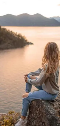 Enhance your phone's look with a stunning live wallpaper featuring a woman on a rock overlooking water