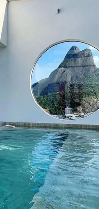This incredible phone live wallpaper showcases a crystal-clear swimming pool amidst a lush green landscape with a striking view of a grand mountain range