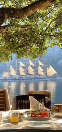 This phone wallpaper features a wooden table with a plate of food on top, a hanging picture frame, and a sailing boat in the distance