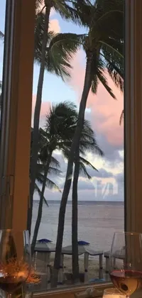 This live wallpaper depicts glasses of wine on a table, with a painting on the wall and a beautiful view of palm trees swaying outside the windows