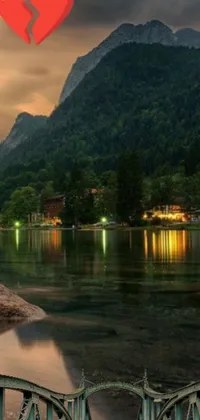 This live phone wallpaper displays a romantic and picturesque evening scene of a bridge over a serene body of water in Slovenia, with stunning mountains in the background