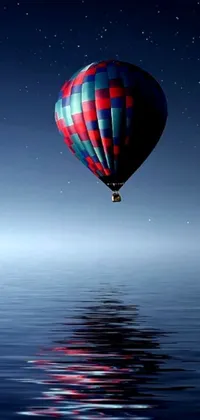 This live wallpaper showcases a gorgeous hot air balloon floating above a serene body of water, surrounded by a dark mountain range in the distance