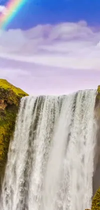 This live wallpaper depicts a stunning waterfall with a rainbow in the background, set against a lush green landscape