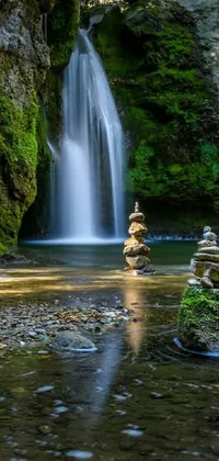 This phone live wallpaper showcases a serene waterfall flowing through a lush green forest, with a stunning sculpture made of stacked stones situated at its base