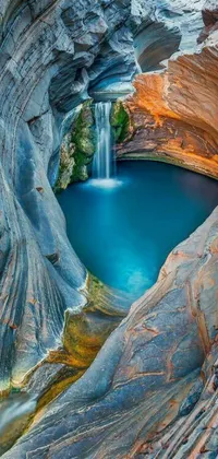 This phone live wallpaper depicts a stunning waterfall located in a canyon with crystal blue waters and vibrant rocks