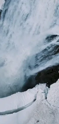 This live mobile wallpaper displays a breathtaking video art of a man standing beside a waterfall in a snowy landscape