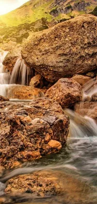 This phone live wallpaper showcases a picturesque mountain range with a serene stream of water flowing between rocks
