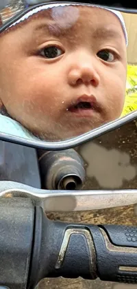 This phone live wallpaper features an intense close-up photograph of a baby sitting on a motorcycle's mirror with a horrified expression