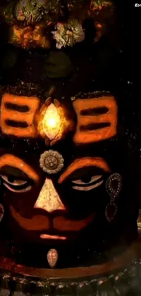 This dynamic phone live wallpaper features a close-up of a detailed mask resting on a table, complemented by a vibrant cave painting, mystical black aura, and intricate rendering of Kalighat Hanuman's head