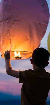 This live wallpaper for your phone displays a beautiful and serene scene of a cute boy holding a sky lantern up in the air