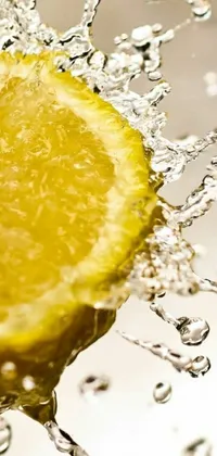 This lively phone wallpaper features a yellow lemon being dropped into a shimmering water fountain surrounded by bubbles