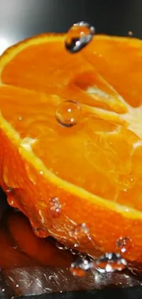 This phone live wallpaper features a slice of orange on a cutting board with a water droplet