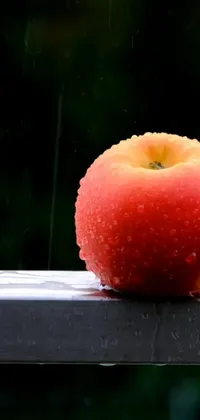 Adorn your smartphone screen with this high quality 4k live wallpaper of a red apple and orange fruit placed on a wooden table, in the midst of a rainy background captured in great detail by Niko Henrichon