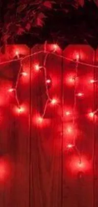 Get into the festive spirit with this phone live wallpaper featuring red Christmas lights hanging from a wooden fence in a chauvet pattern