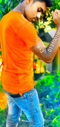 This phone wallpaper showcases a striking young man with a tattoo on his arm in an orange t-shirt