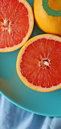 This live phone wallpaper features three halves of grapefruits resting on a blue plate
