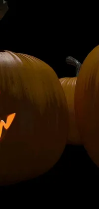 This live wallpaper features a spooky digital rendering of two intricately carved pumpkins illuminated by candlelight