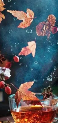 This phone live wallpaper captures the essence of autumn with a still life of a cup of tea on a wooden table surrounded by falling leaves and berries
