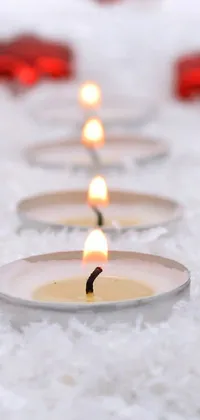 This stunning phone live wallpaper showcases a group of flickering candles placed amidst a setting of snowfall