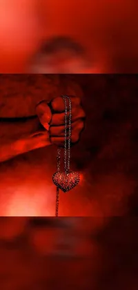 This striking phone live wallpaper captures a heartfelt moment featuring a person holding a chain with a heart