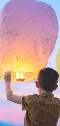 Get lost in a magical scene with this stunning phone live wallpaper! A young boy holds a beautifully lit sky lantern, providing a warm and enchanting glow to the surroundings