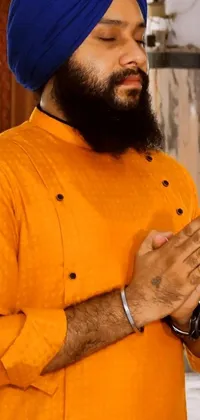 This intriguing live wallpaper features a man wearing a blue turban in a kitchen, sporting an orange prison jumpsuit and gold jewelry while holding his hands together in prayer