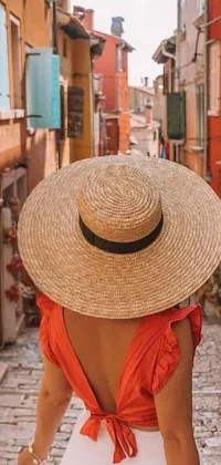 This phone live wallpaper showcases a mesmerizing image of a woman walking down a charming cobblestone street wearing a chic straw hat