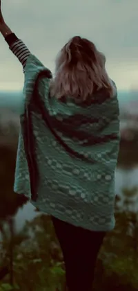 This live wallpaper displays a tranquil scene of a woman on a green hillside in a tartan cloak