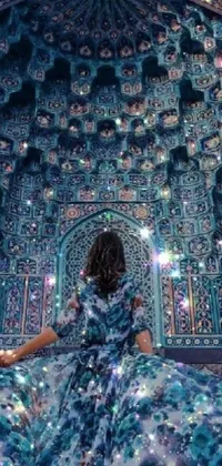 This phone live wallpaper features a mesmerizing design of a woman in a flowing blue dress standing in front of a vivid blue wall with intricate designs and shimmering sparkles