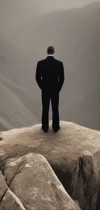 This phone live wallpaper features a striking and surreal image of a man standing on top of a large rock formation