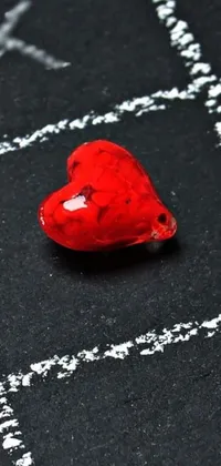 This stunning phone live wallpaper showcases a bold red heart resting on a sleek black surface surrounded by a multicolored glass bead game pattern