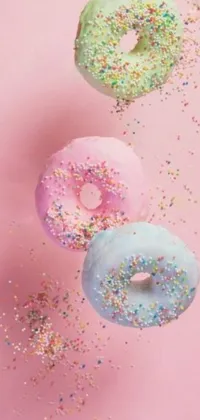 This phone live wallpaper features three mouth-watering donuts with colorful sprinkles against a bright pink background