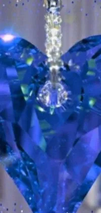 This phone wallpaper showcases a close-up image of a single sugar crystal with a beautiful blue heart ornament hanging from a window in the background