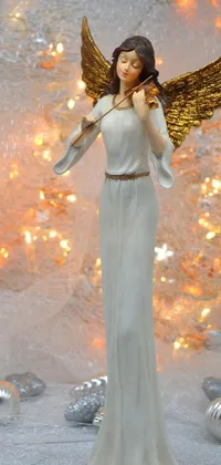 This elegant and festive live wallpaper features a white figurine of an angel standing tall in front of a Christmas tree
