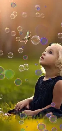 This enchanting live wallpaper portrays a cute little girl sitting in green grass and blowing vibrant bubbles of all sizes and shapes