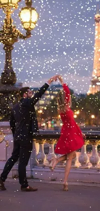 This live wallpaper depicts a charming evening scene before the iconic Eiffel Tower, as a couple dances together - the woman wearing a striking red dress that pops against the warm lighting