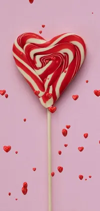 Decorate your phone with a playful and eye-catching live wallpaper featuring a delightful red and white heart-shaped lollipop on a stick