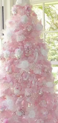 This live wallpaper depicts a fully decorated pink Christmas tree in front of a snowy window