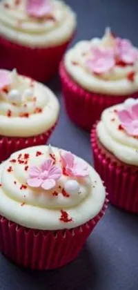 This phone wallpaper showcases a scrumptious close-up of cupcakes with white frosting and pink flowers on a wooden table