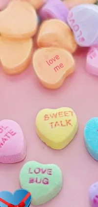 This live wallpaper features a pile of conversation hearts in pastel colors, arranged on a table and coated in candy messages
