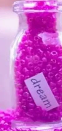 This phone live wallpaper showcases a stunning jar filled with captivating pink beads resting gracefully on a table, accompanied by purple tubes in a close-up view