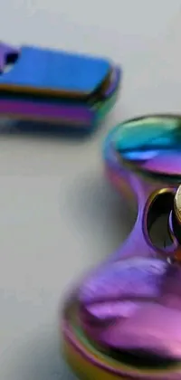 This phone wallpaper features a hyperrealistic, colorful fidget spinner atop a smoothly polished metal table