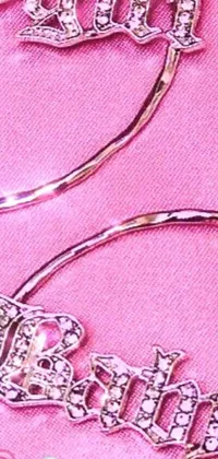 This live phone wallpaper depicts a luxurious pair of hoop earrings set against a pink background
