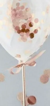 Looking for a fun, playful phone wallpaper? Check out this live wallpaper of a rose gold balloon filled with confetti! As the background, you'll find a sheer design made up of small dots, adding a dreamy touch to the overall look