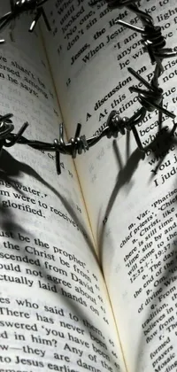 This phone live wallpaper features a powerful image of a barbed wire crown resting on top of an open book, adorned with gothic harts