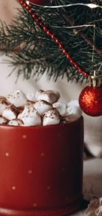 Get into the holiday spirit with this beautiful phone live wallpaper featuring a red mug of steaming hot chocolate topped with fluffy marshmallows, surrounded by a festive Christmas tree