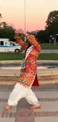 Add some color and energy to your phone's home screen with this live wallpaper! Featuring a vibrant man in a multicolored jacket dancing in front of a stunning fountain, this wallpaper is sure to grab attention