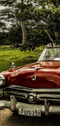 This phone live wallpaper depicts an old red convertible parked alongside a winding road